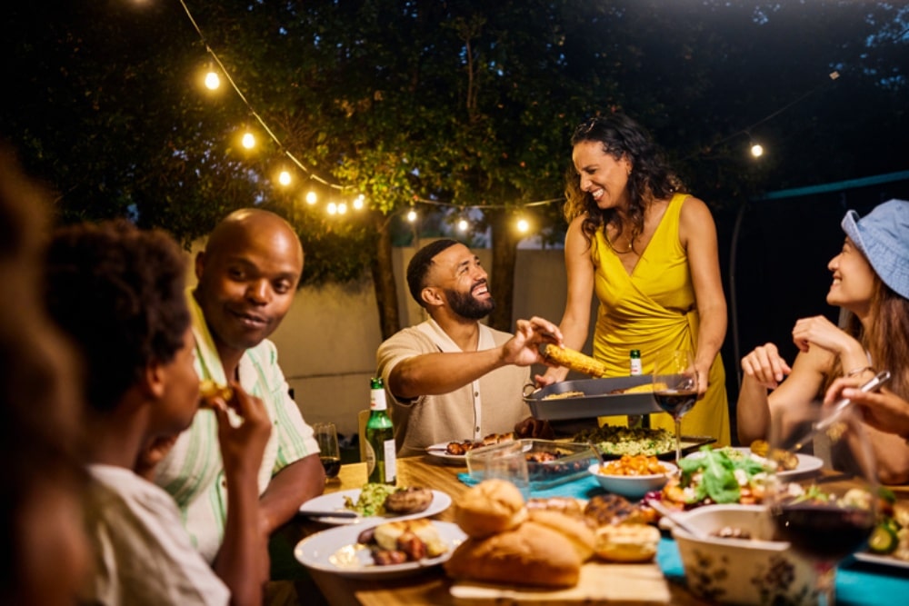 Group of people enjoying food together at outdoor gathering with string lights
