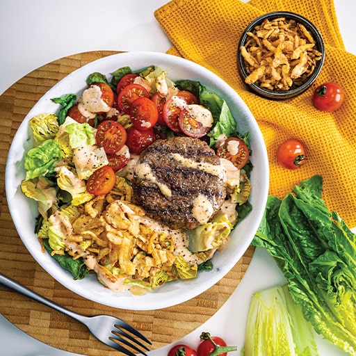 Burger-inspired salad bowl with beef, vegetables and dressing
